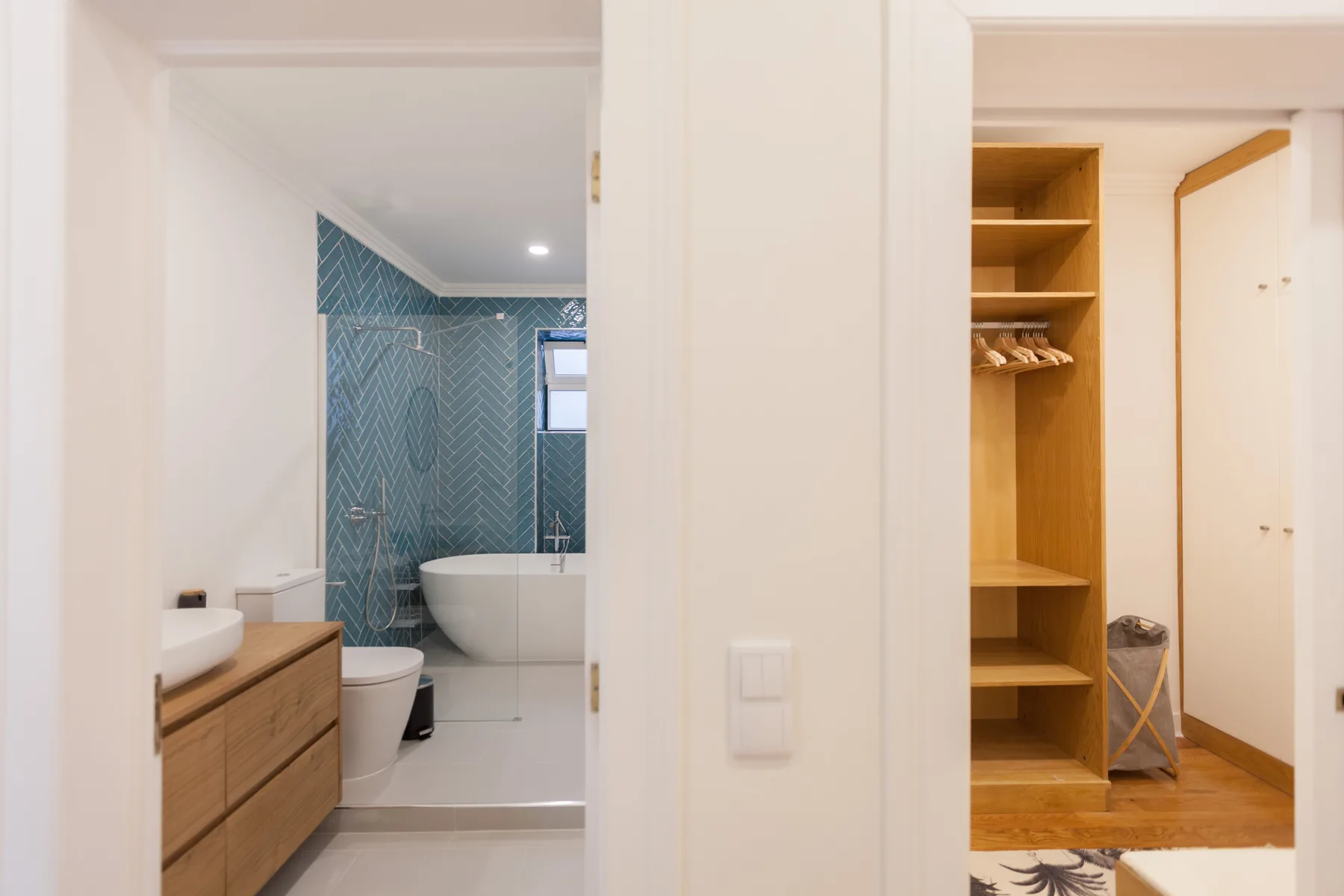 A bathroom with blue patterned tile is visible beside an open wooden shelving area.