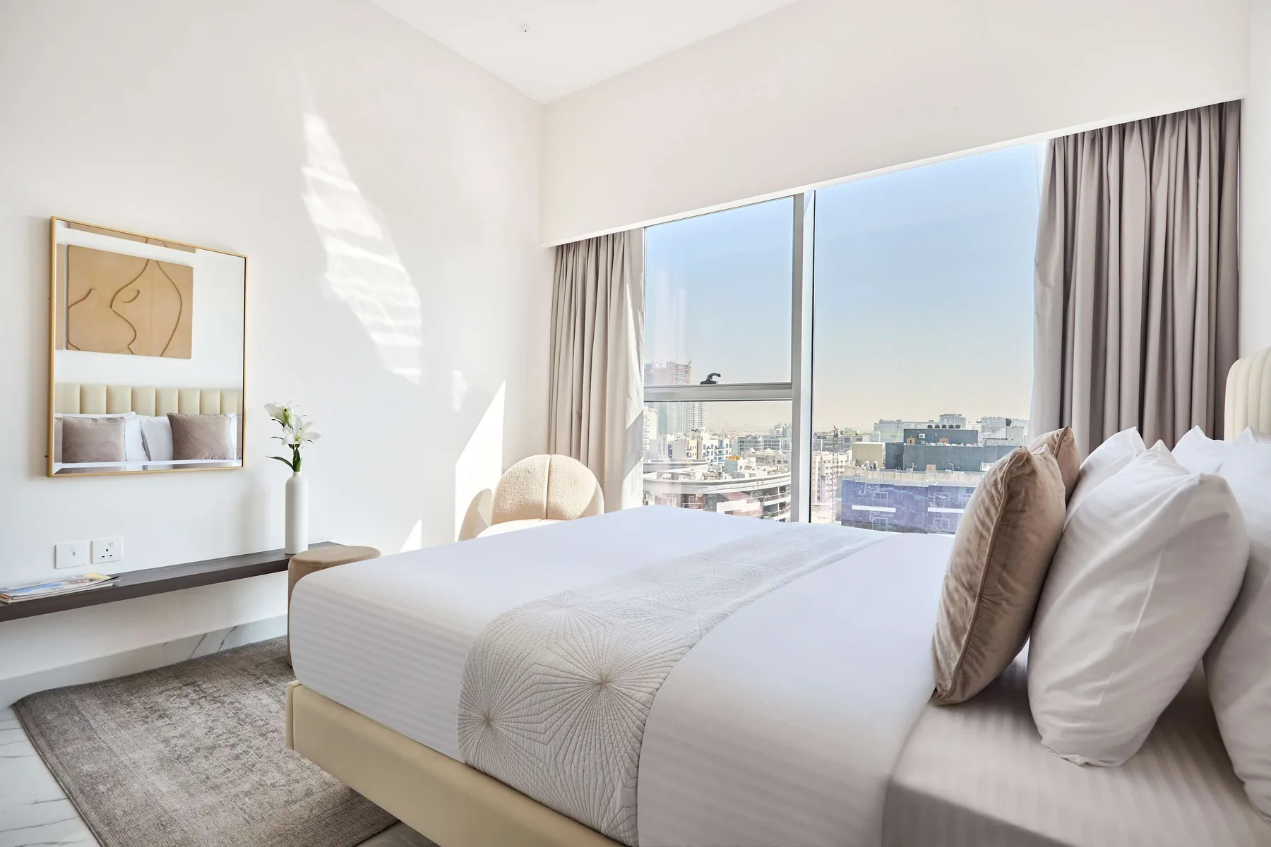 Un dormitorio luminoso con una cama bien tendida junto a una gran ventana.