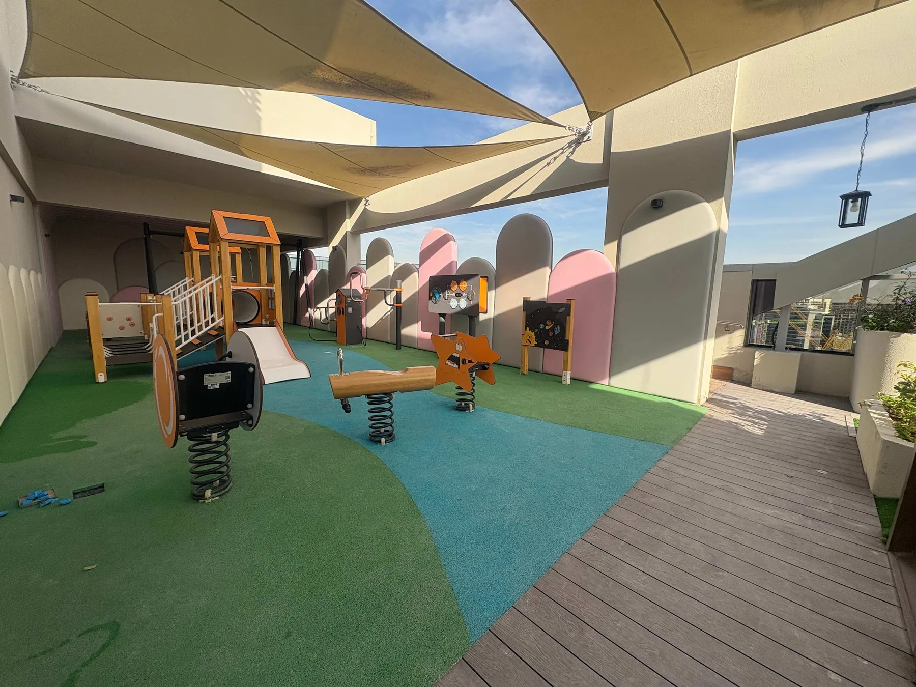 Un parque infantil al aire libre tiene juegos coloridos bajo grandes toldos de sombra.
