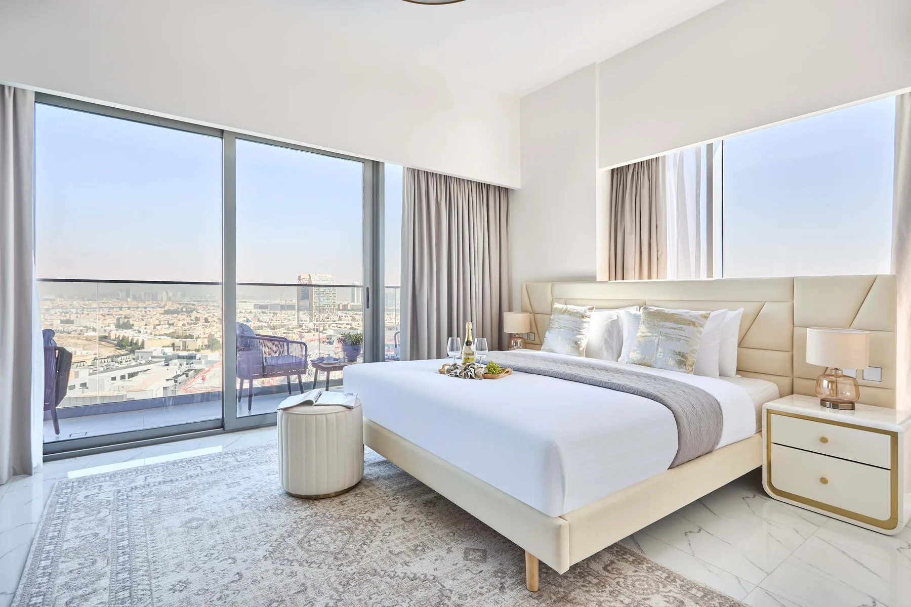 Un dormitorio luminoso con una cama grande junto a ventanales con vistas a la ciudad.