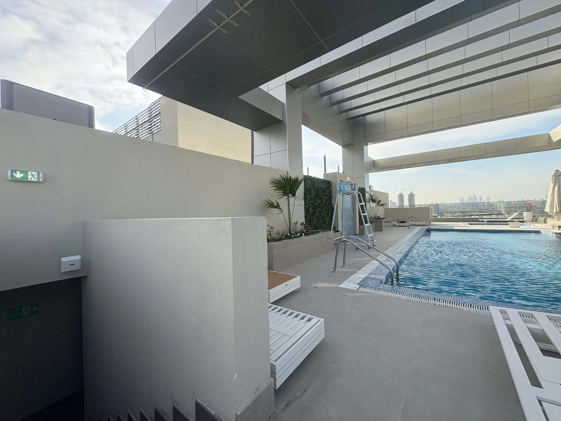 Una piscina en la azotea junto a una terraza pavimentada, con el perfil urbano a lo lejos.