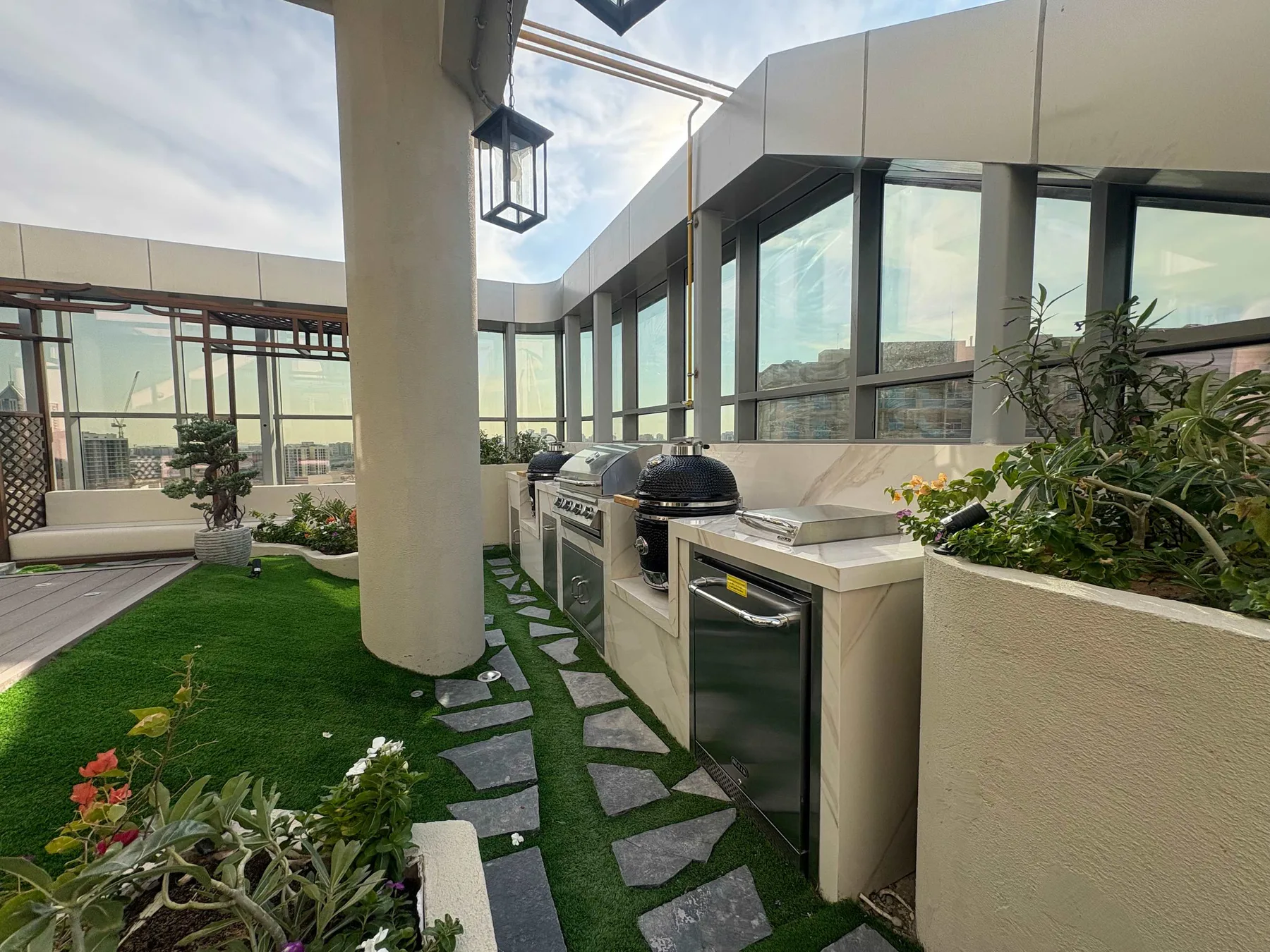Terraza en la azotea con una encimera para cocinar al aire libre, plantas y grandes ventanales.