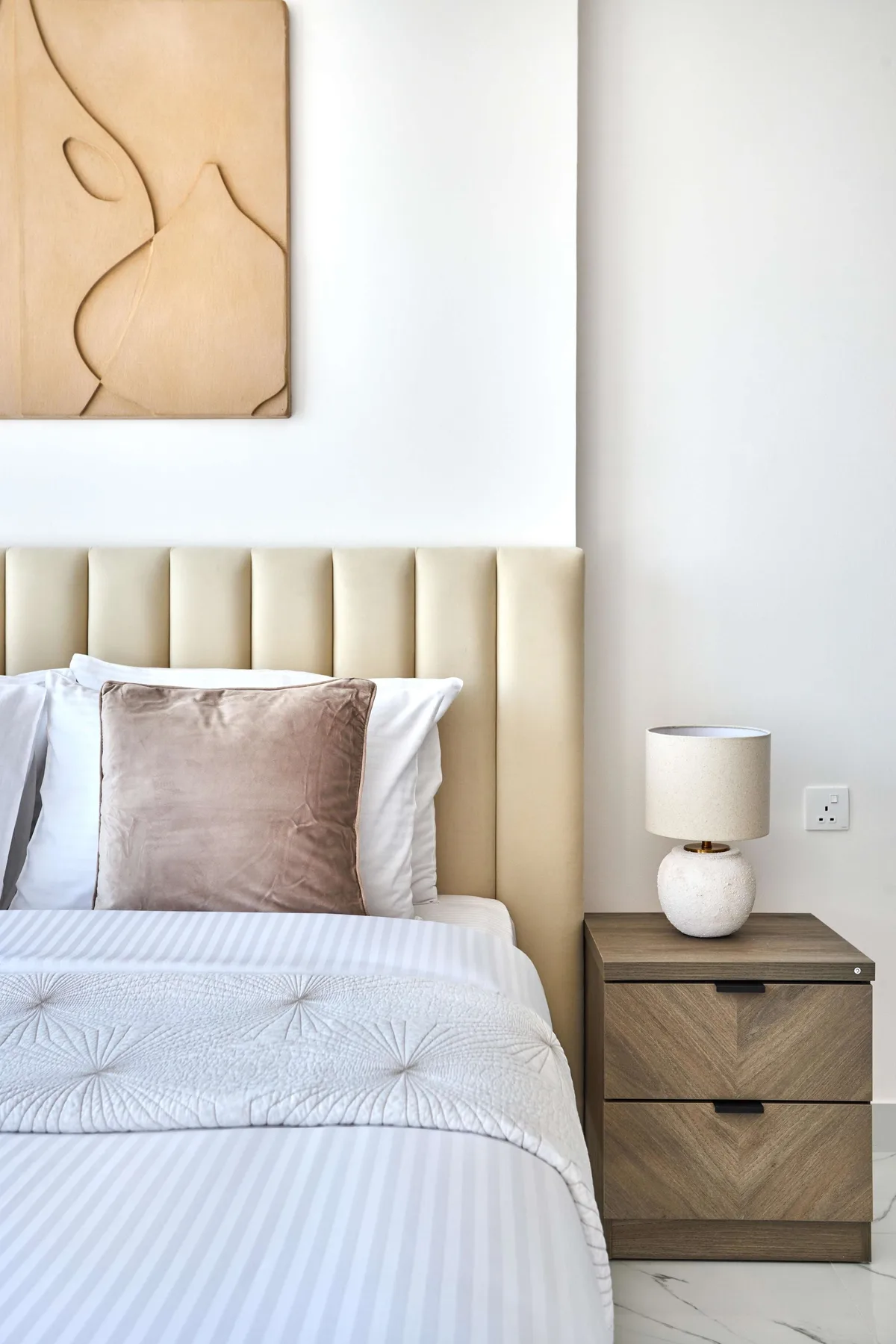 Una cama bien arreglada con una mesa de noche y arte abstracto en la pared.