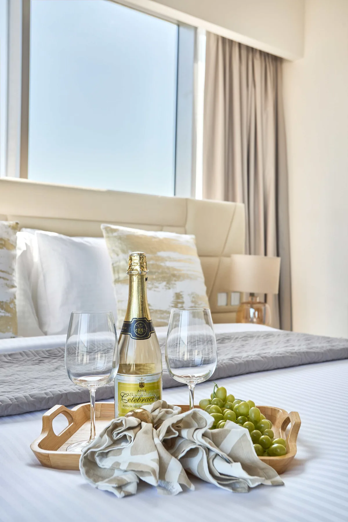 Un dormitorio con una cama, almohadas y una bandeja con uvas y vino espumoso.