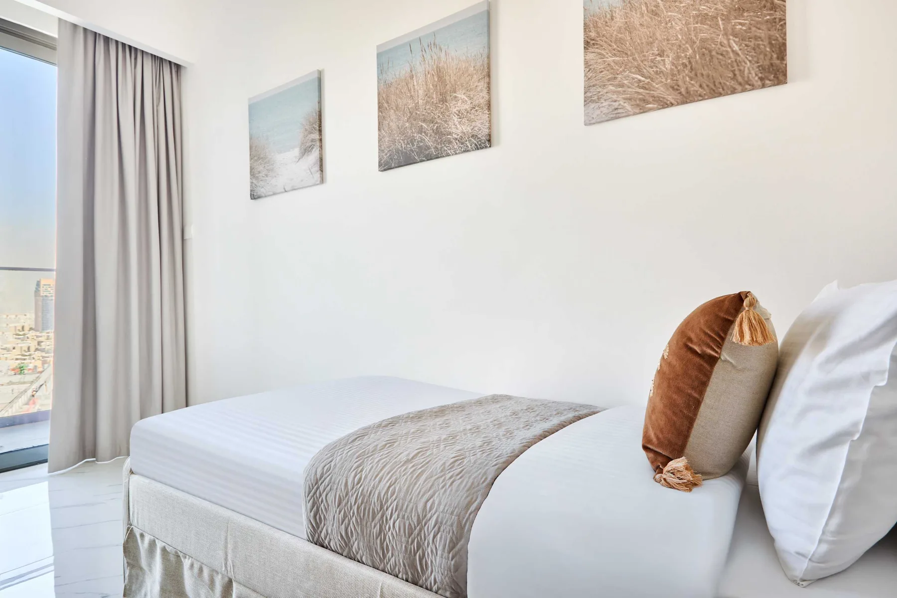 Un dormitorio luminoso con una cama bien arreglada y láminas de paisajes en la pared.