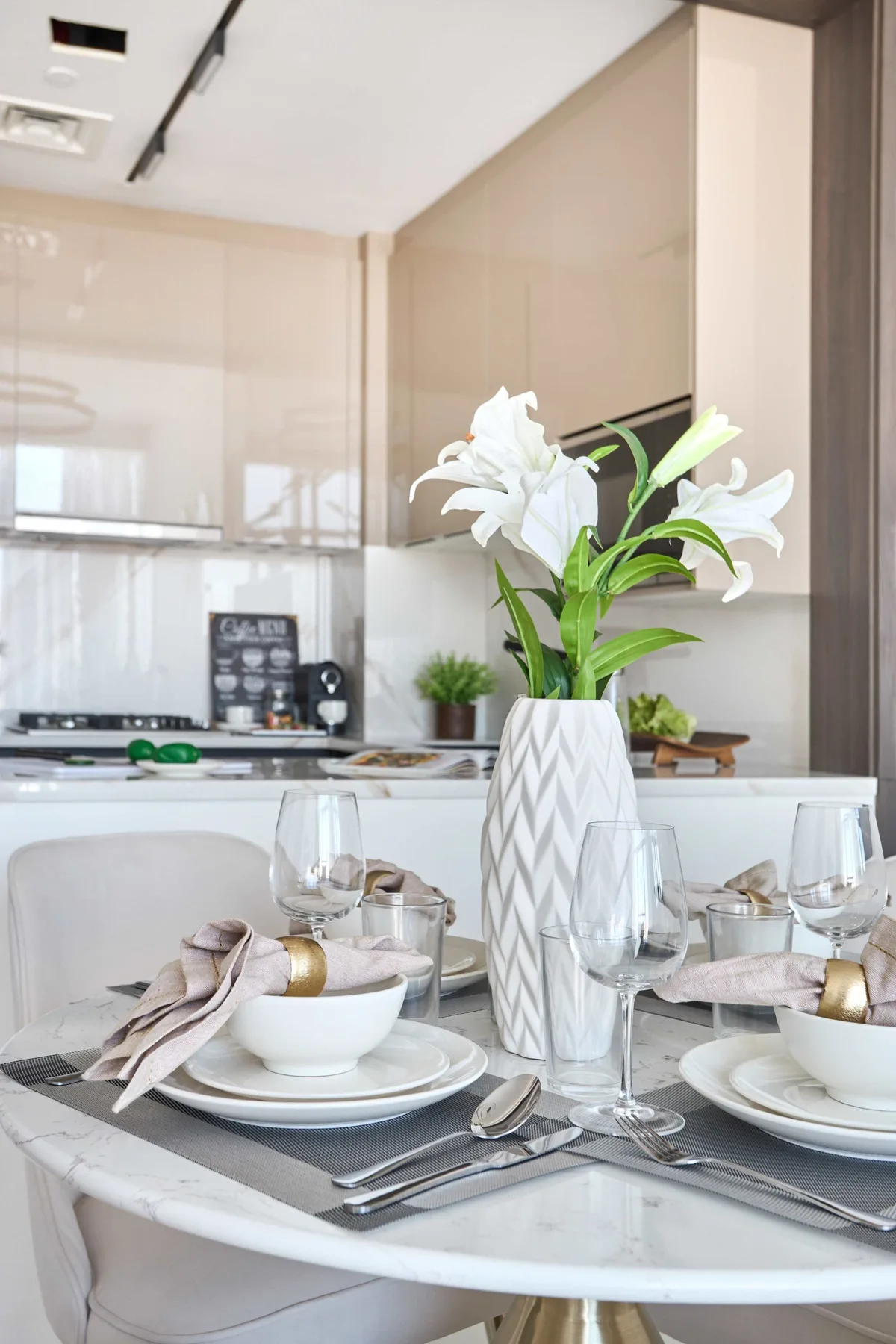 Una mesa de comedor está preparada con platos y un jarrón de flores blancas.