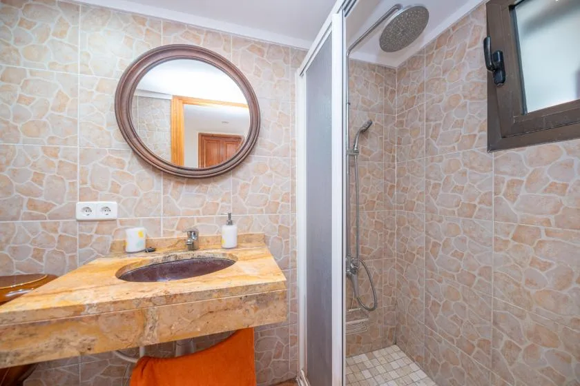 Un baño alicatado con lavabo de piedra, espejo redondo y ducha de vidrio.
