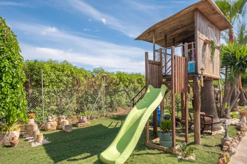 Una zona de juegos en el patio con una casita de madera y un tobogán verde.