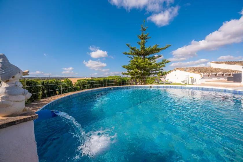 Una piscina al aire libre con una fuente, junto a un árbol y edificios bajos.