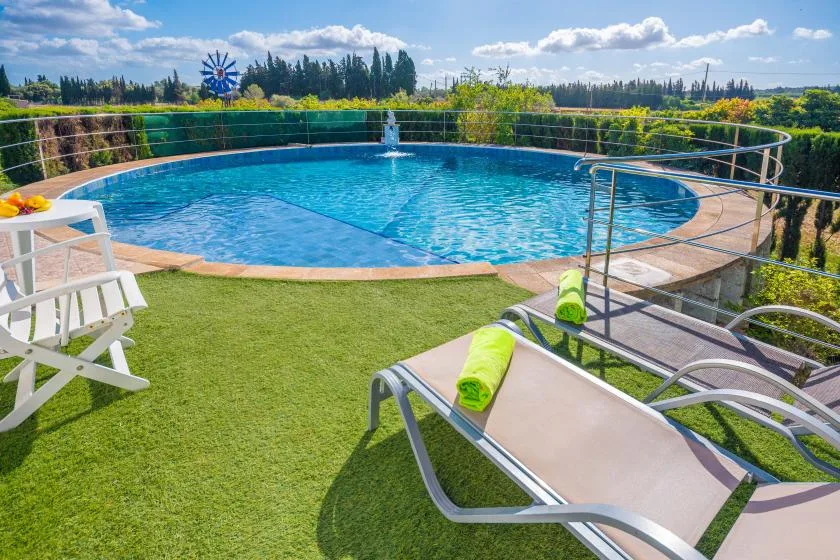An outdoor swimming pool surrounded by lawn and greenery.
