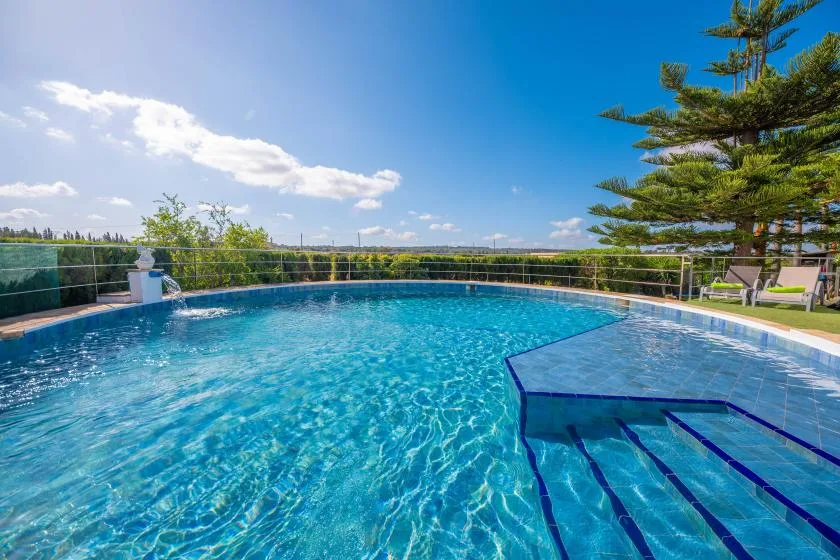 Una piscina al aire libre con agua azul clara y árboles junto al borde.