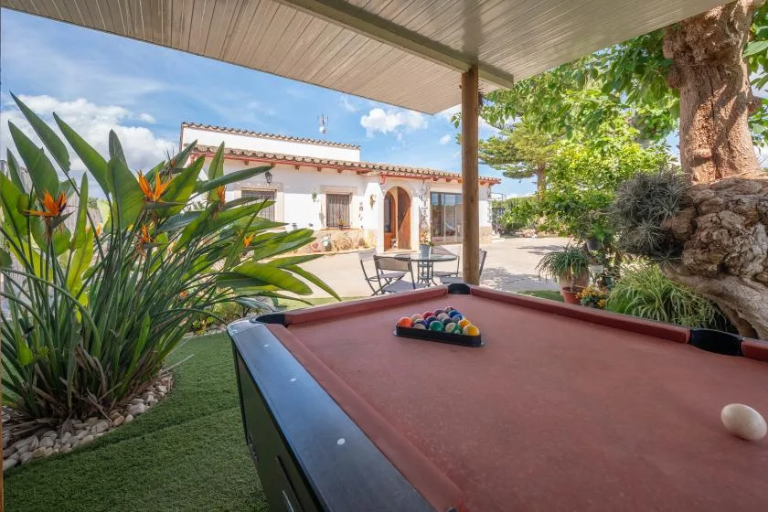 Una mesa de billar al aire libre y cubierta está junto a un patio y un jardín.