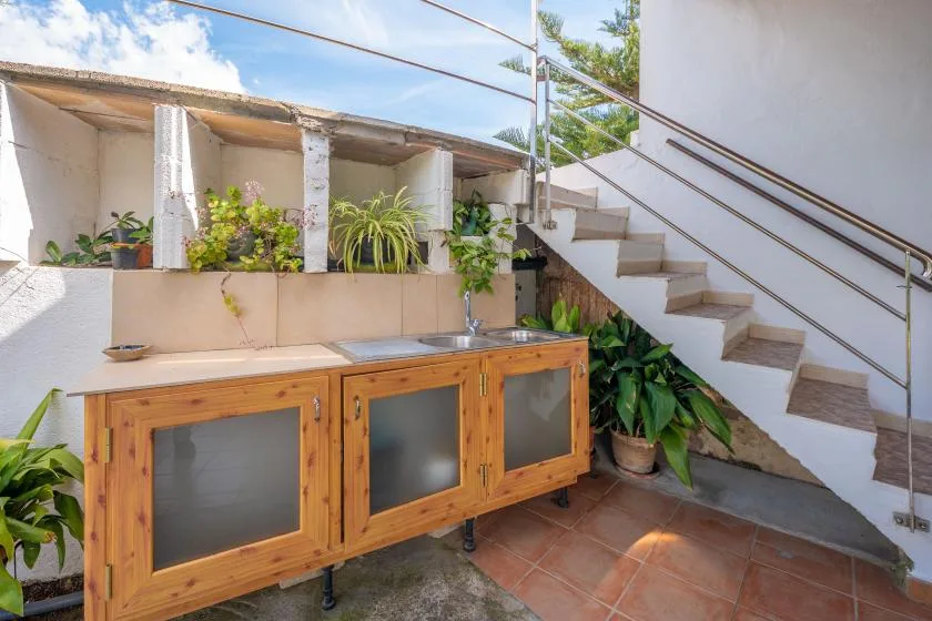 Una escalera exterior junto a un mueble de madera y plantas en macetas.