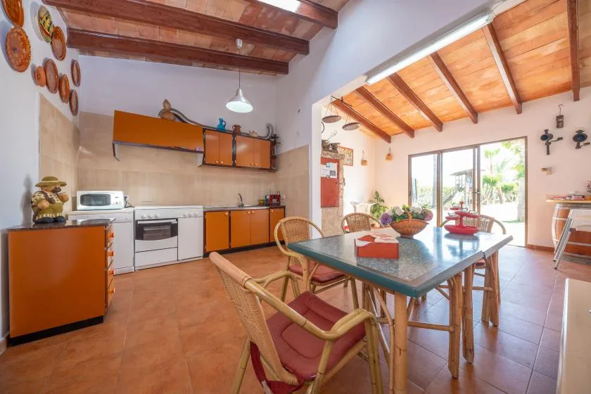 Una cocina y comedor con vigas de madera en el techo y una mesa de comedor de vidrio.