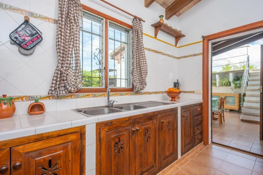 Una cocina con azulejos, una encimera larga, armarios de madera y un fregadero bajo las ventanas.