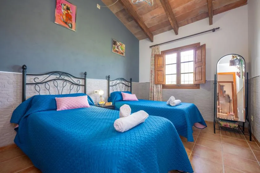 Un dormitorio con dos camas vestidas con ropa de cama azul bajo un techo de madera.