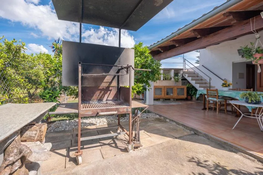Un patio exterior con una parrilla metálica, asientos y escaleras junto a la casa.