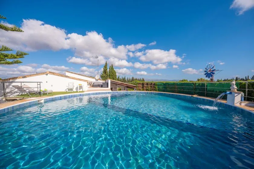 Una piscina al aire libre está junto a un edificio bajo, bajo un cielo azul.