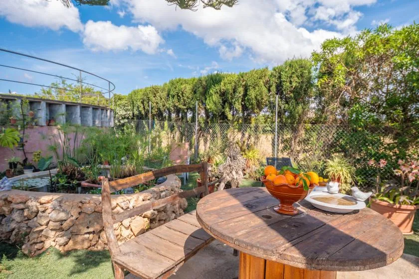 Un patio al aire libre con una mesa redonda de madera con fruta y platos.
