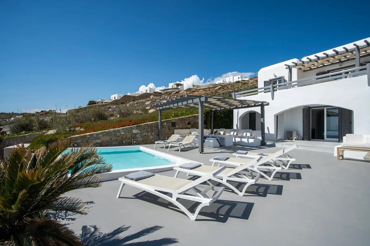 A poolside terrace with lounge seating beside a white villa.