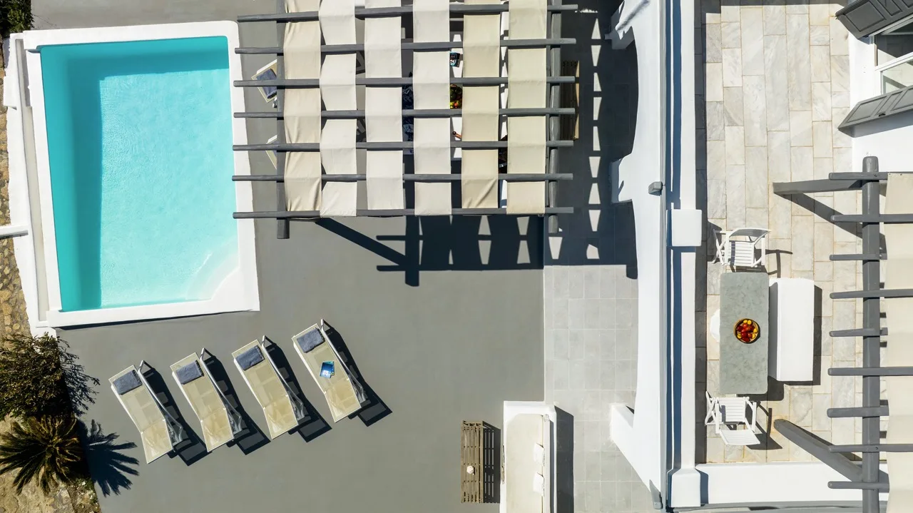 An aerial view shows a turquoise pool, lounge chairs, and a pergola.