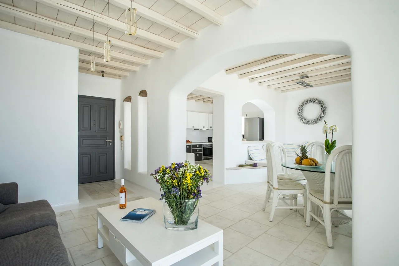 A bright living and dining area with white seating and a vase of flowers.