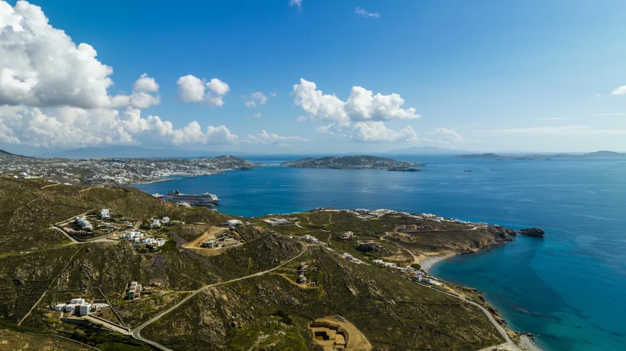 Aerial view of a rugged coastline with blue water and scattered buildings.