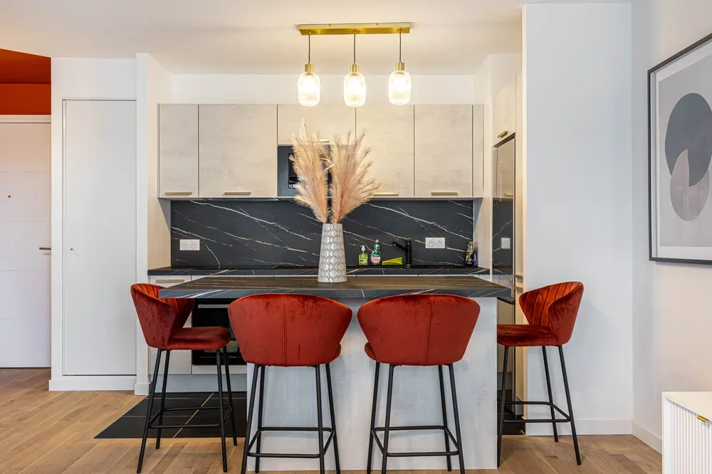 Una cocina moderna con isla central, asientos de barra y lámparas colgantes.
