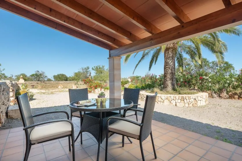 Un patio cubierto tiene una mesa de comedor y asientos con vistas a un jardín.