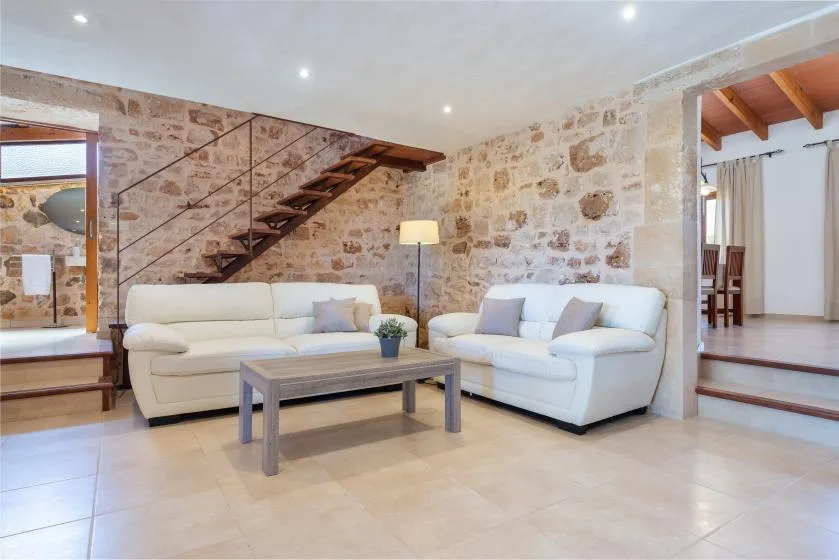 Una sala luminosa con asientos blancos y una escalera de madera junto a paredes de piedra.