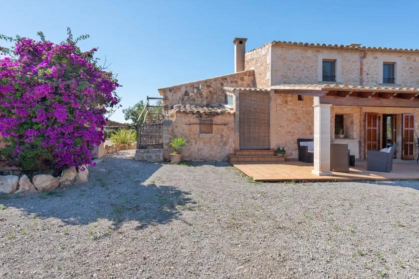 Una casa de piedra con un patio cubierto está junto a un arbusto en flor.