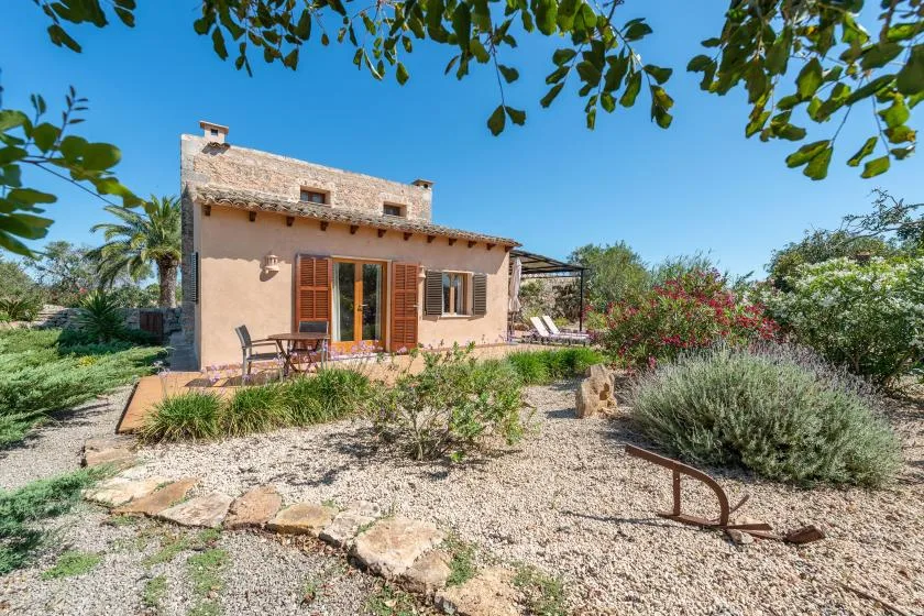 Una casa pequeña da a un jardín de grava, con asientos al aire libre cerca de la entrada.