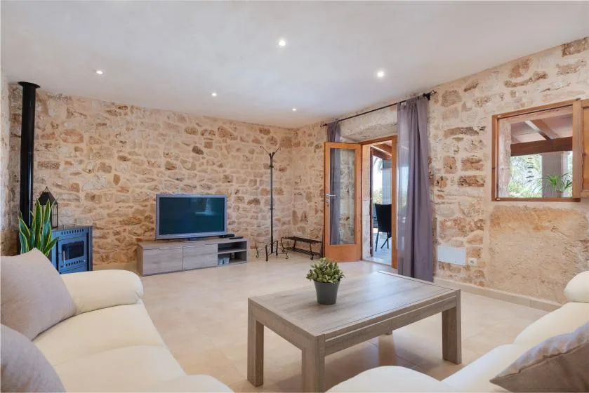 Una sala de estar con paredes de piedra, asientos, un televisor y una mesa de centro.