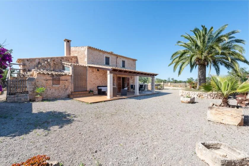 Una casa de piedra con patio cubierto se alza junto a un patio de grava y una palmera.