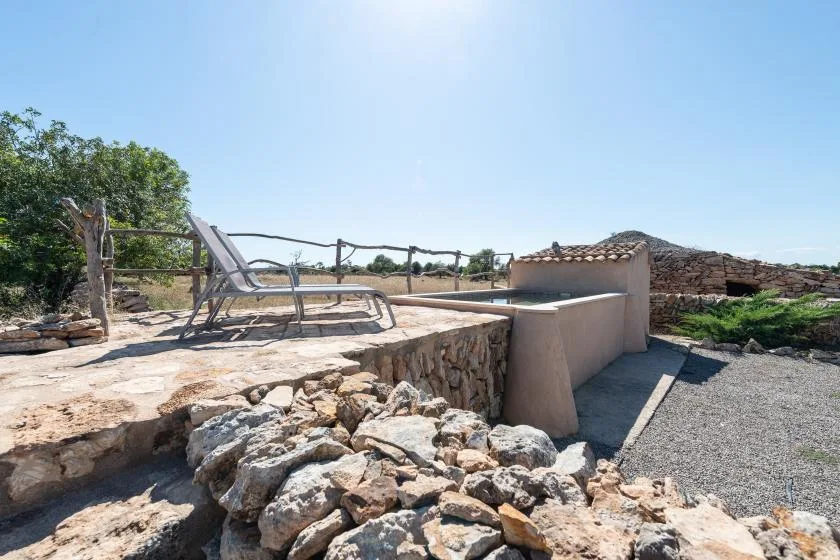 Un patio exterior con asientos reclinables y un muro bajo de piedra.