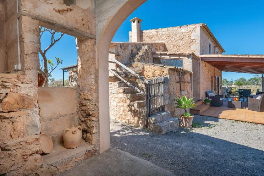 Un patio de piedra con un paso en arco y asientos al aire libre bajo una terraza cubierta.