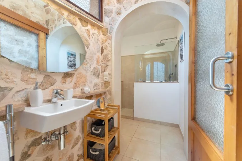 Un baño con paredes de piedra tiene un lavabo junto a una ducha con arco.