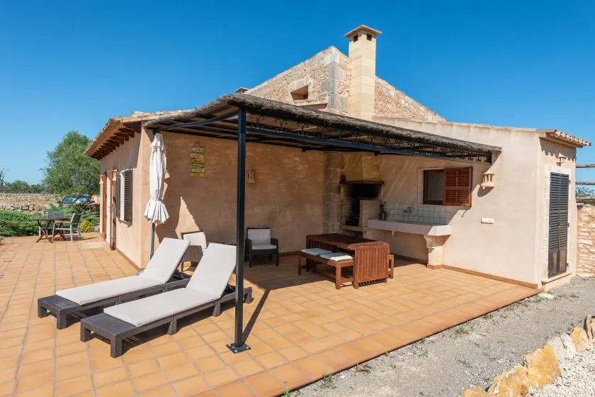 Un patio exterior embaldosado con tumbonas está junto a una zona de comedor a la sombra.