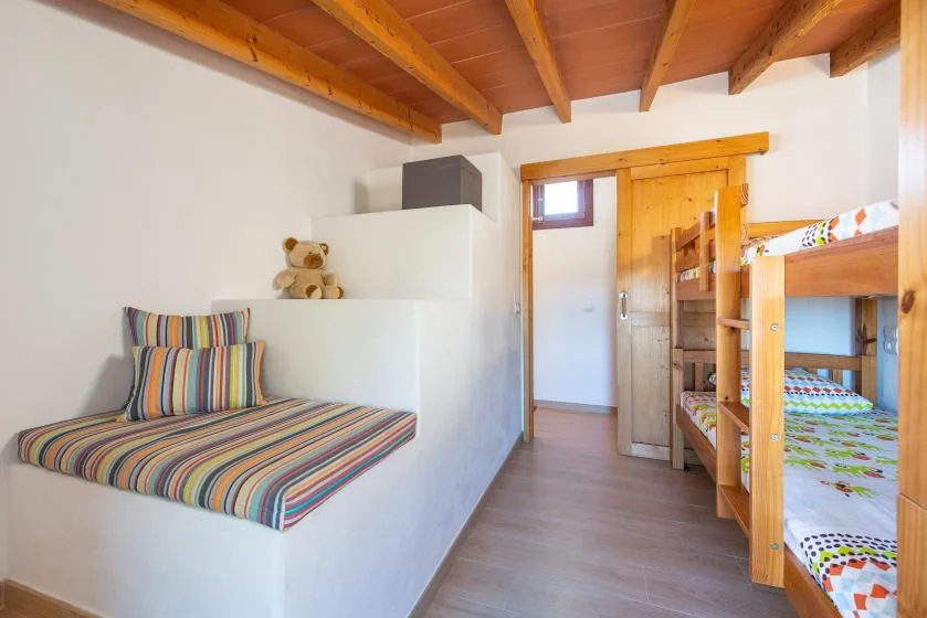 Un dormitorio con asientos a rayas de colores y literas de madera bajo vigas vistas.