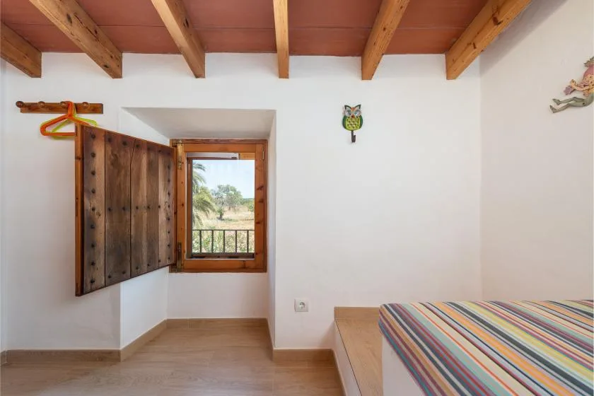 Un dormitorio con una colcha de rayas coloridas junto a una ventana de madera.