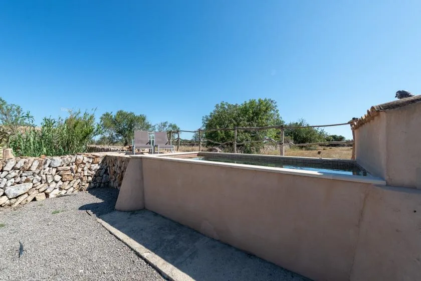 Una piscina al aire libre está junto a un patio de grava y un muro bajo de piedra.
