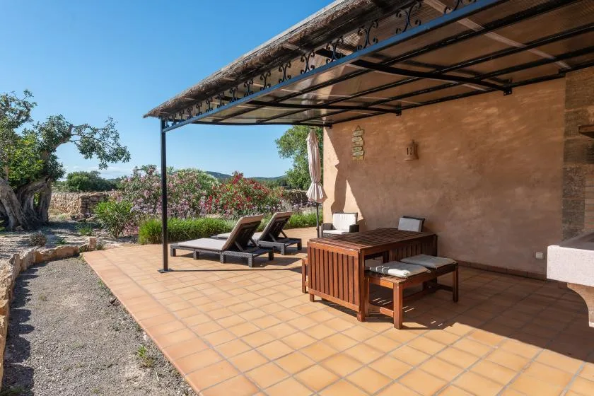 Un patio exterior con suelo de baldosas, comedor a la sombra y asientos de descanso.