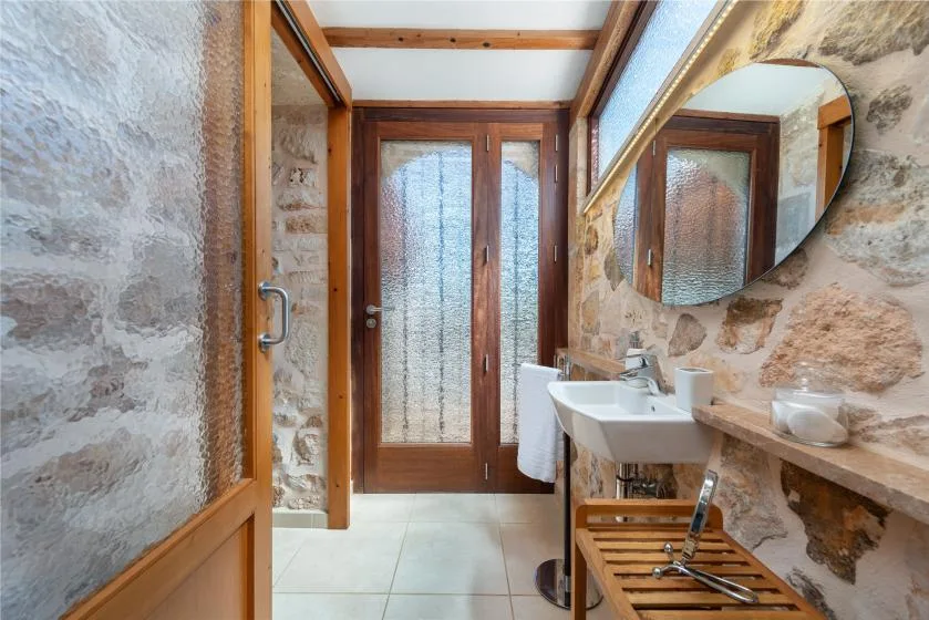 Un baño con paredes de piedra tiene lavabo, espejo y puertas de madera.