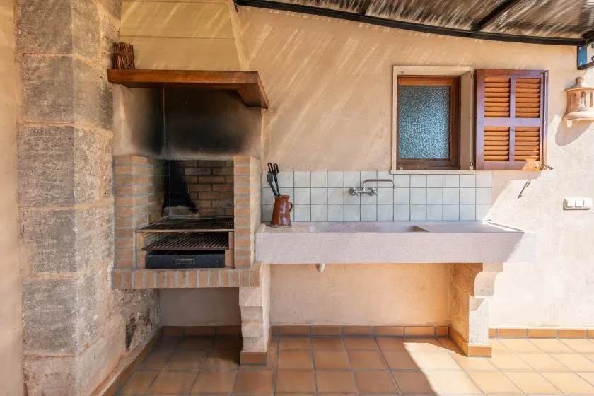Una zona de cocina exterior con una barbacoa de ladrillo junto a una encimera alicatada y un fregadero.
