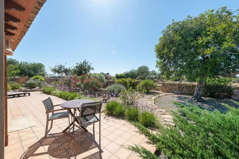 Un patio soleado con una mesa y sillas junto a un jardín ajardinado.