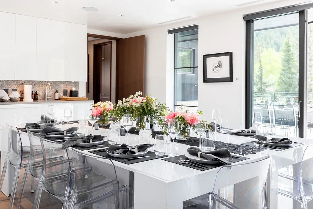A bright dining area has a long table set with dishes and flowers.