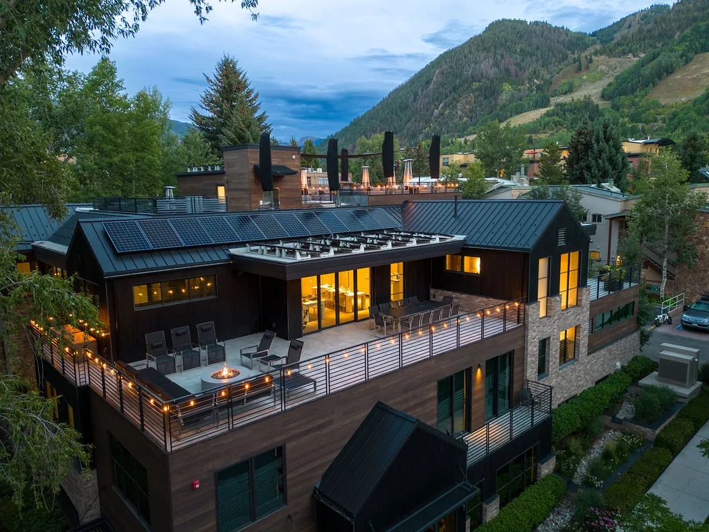 A modern mountain lodge with a broad terrace and wooded hills in the background.