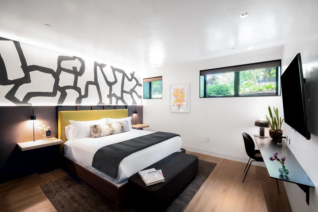 A modern bedroom with a large bed, abstract wall art, and a wide window.