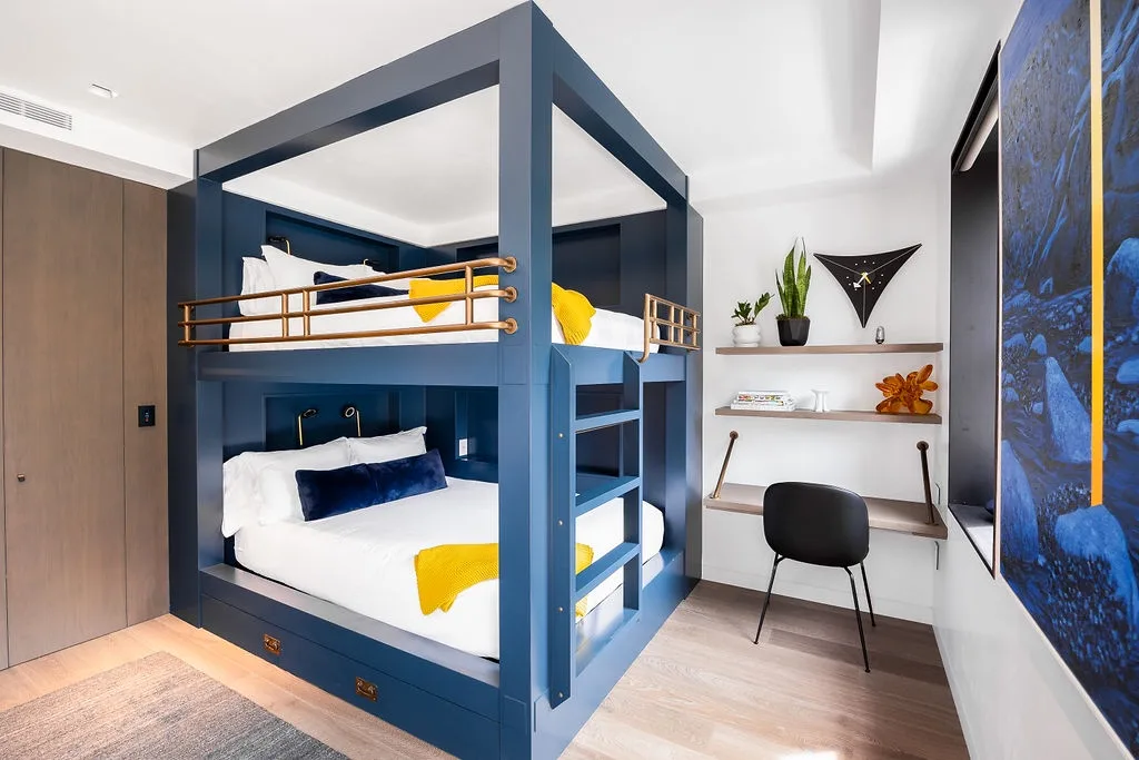 A blue bunk bed sits beside a compact desk with shelves and plants.