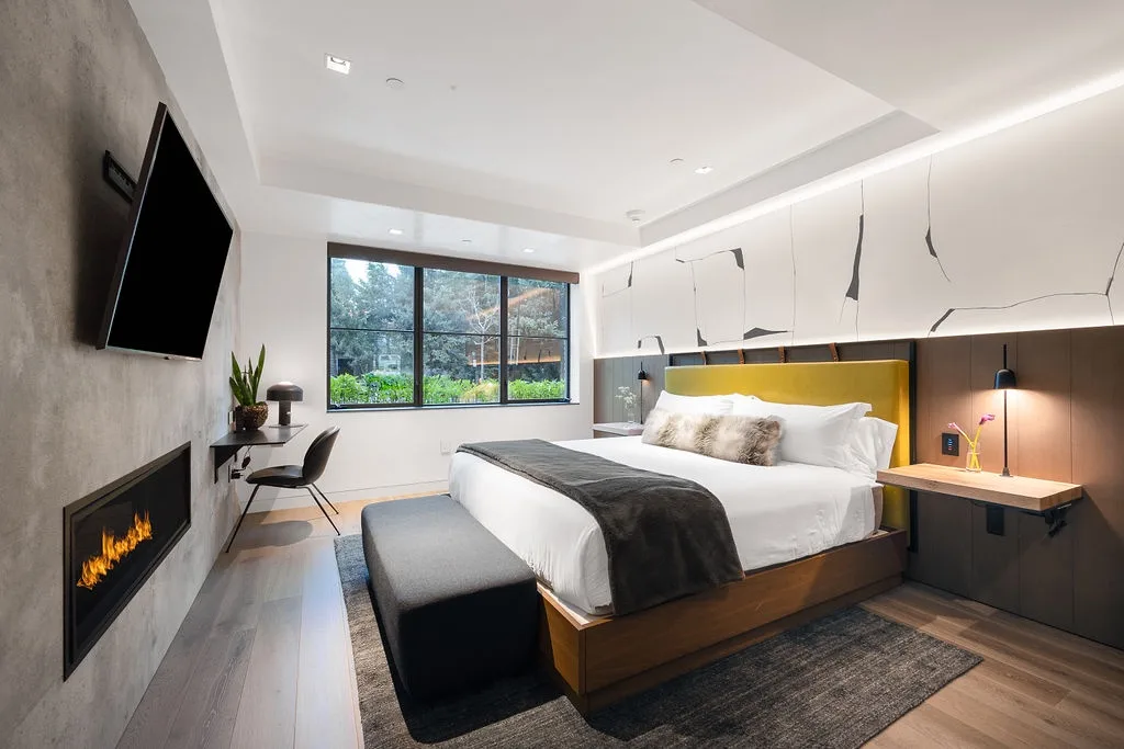 A modern bedroom with a bed, bedside tables, and a large window.